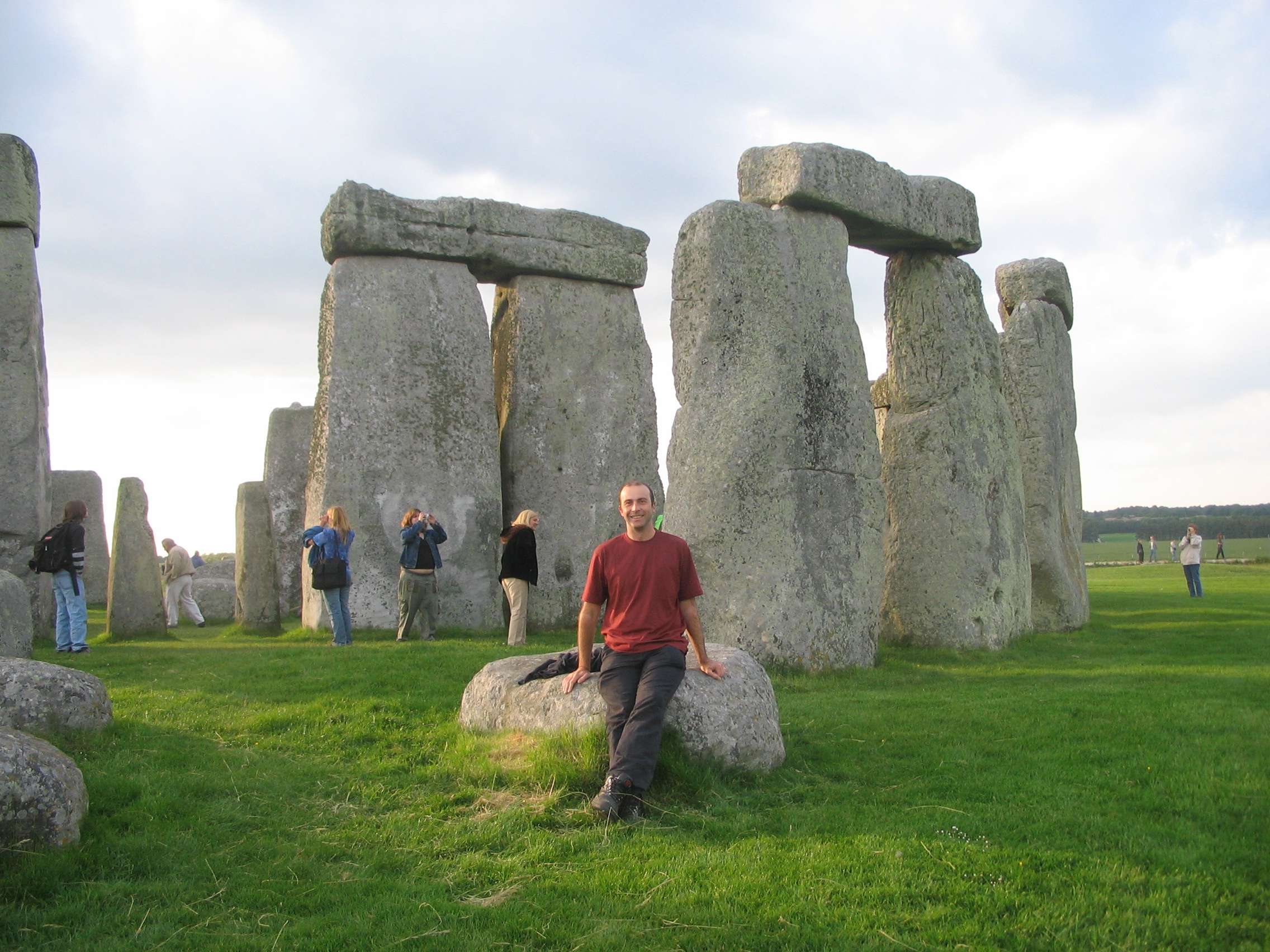 a man sitting on a rock in front of a stone structure with Stonehenge in the background