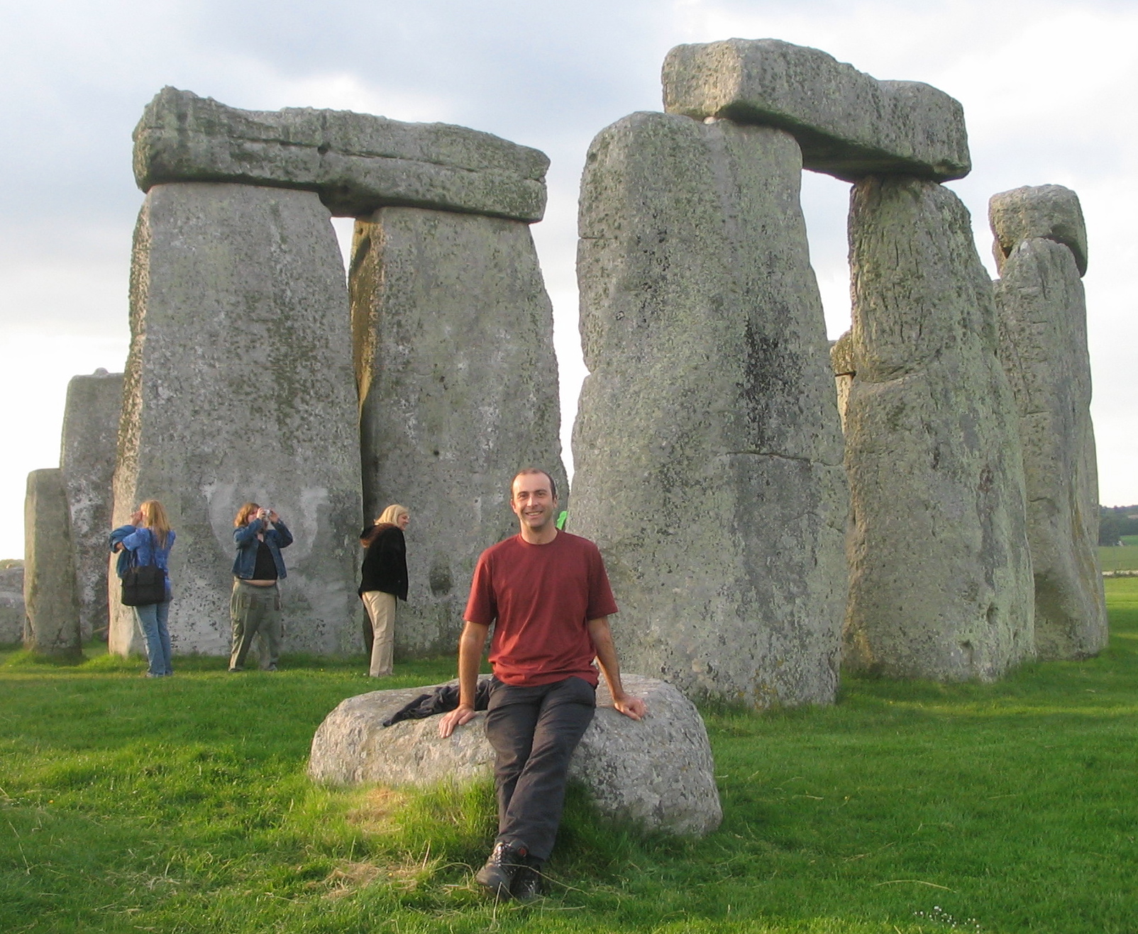 a man sitting on a rock in front of a group of stone structures with Stonehenge in the background