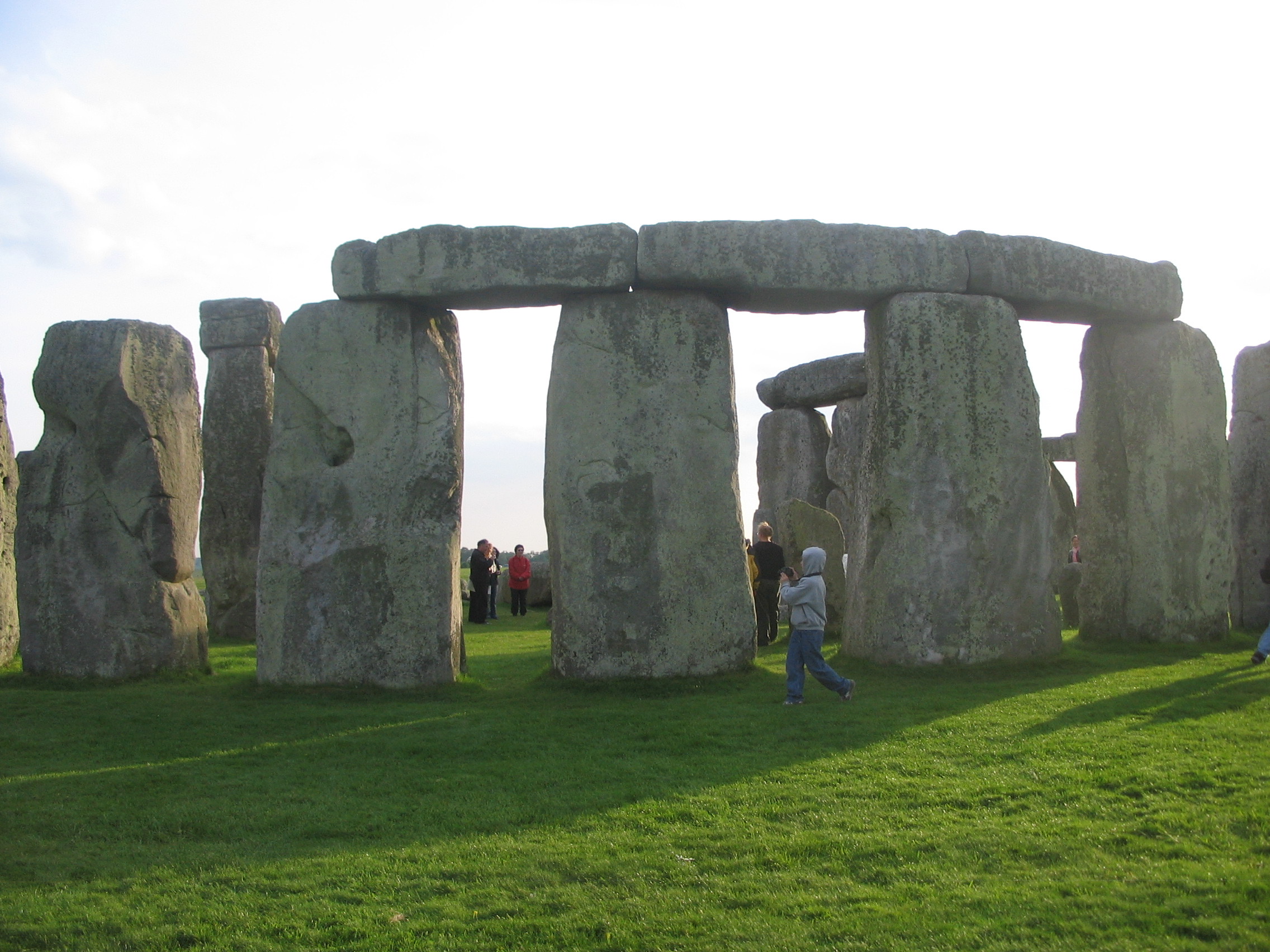 a group of people standing in a grassy area with large stones with Stonehenge in the background