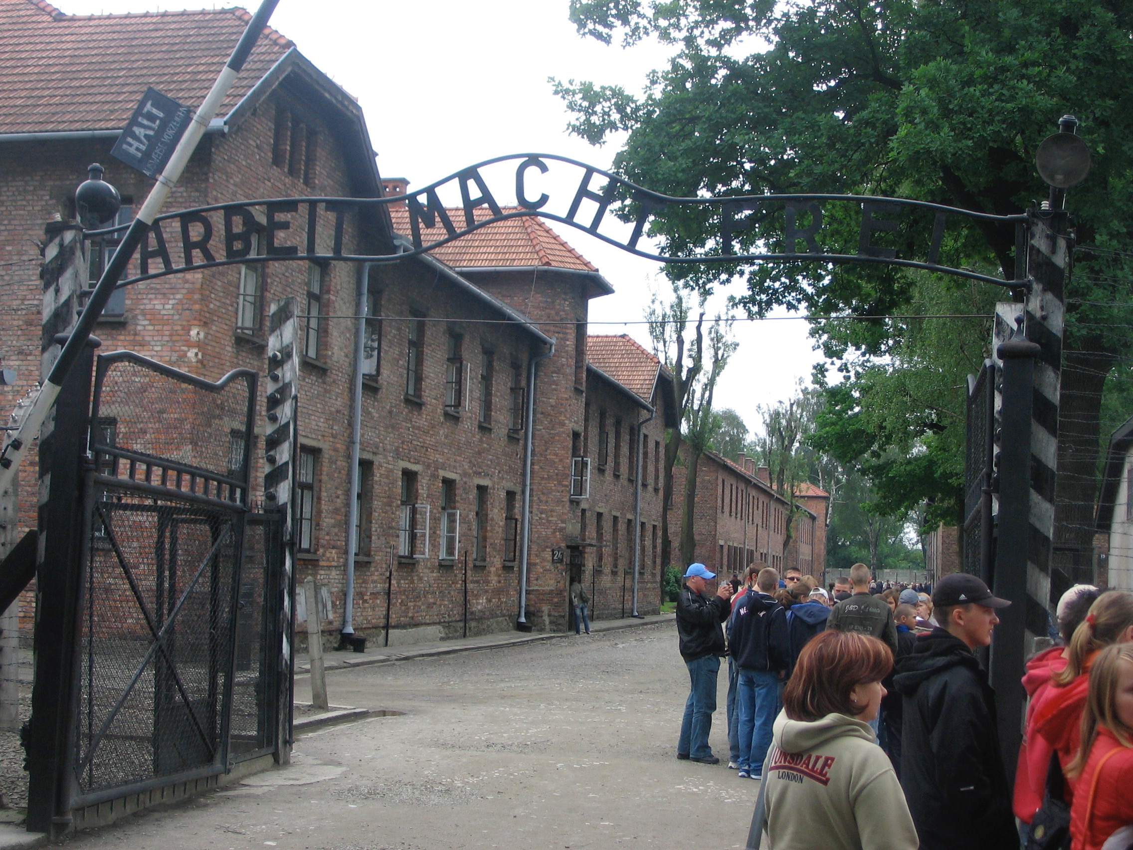 a group of people standing in front of a gate with Auschwitz concentration camp in the background