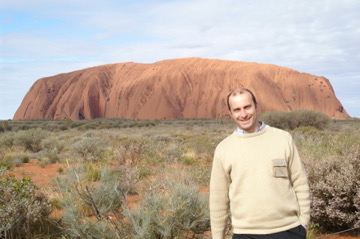 a man standing in a desert with Uluru in the background