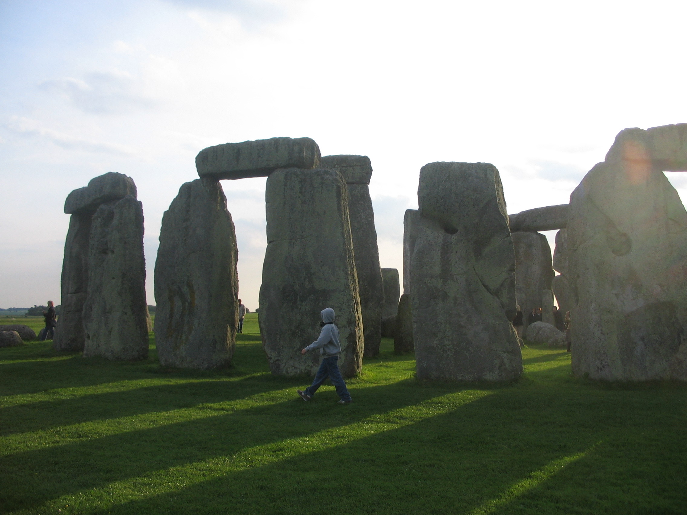 a person walking in a grassy area with large rocks with Stonehenge in the background