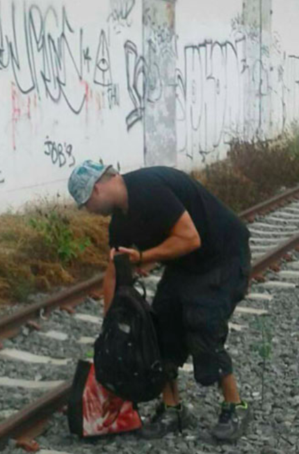 a man looking at a backpack on a train track