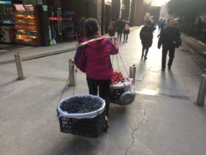 a woman carrying baskets of fruit on a sidewalk