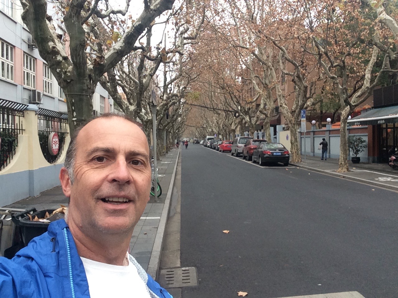 a man taking a selfie on a street with trees and buildings