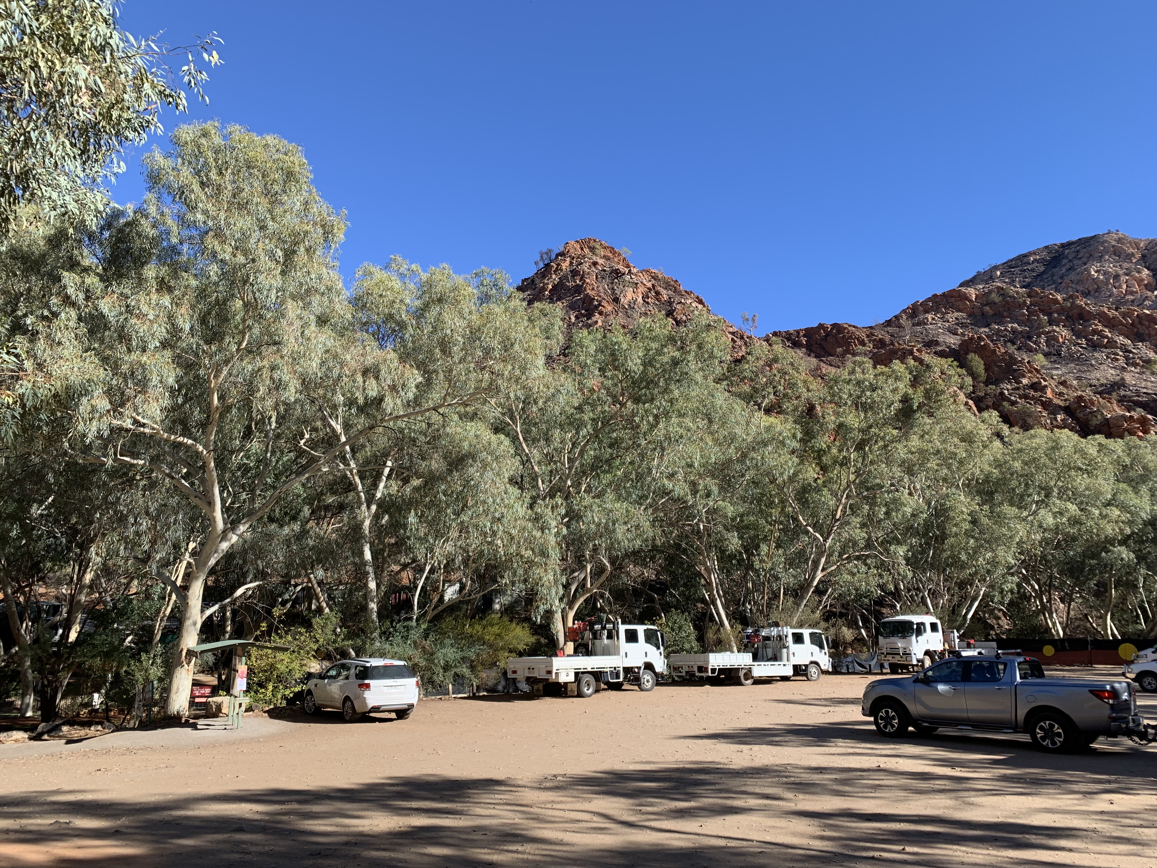 a group of cars parked in a parking lot with trees and mountains in the background