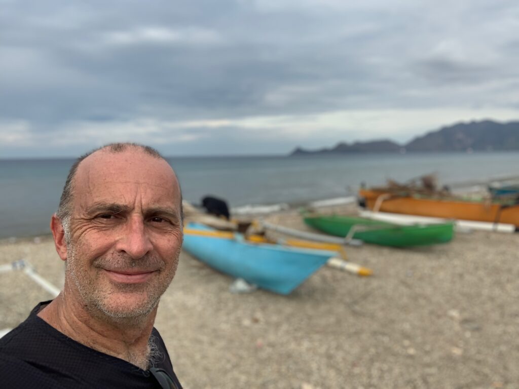 a man taking a selfie on a beach with boats
