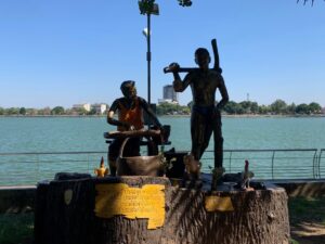 a statue of men on a tree stump next to a body of water