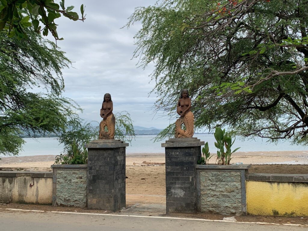 statues on pillars next to a beach
