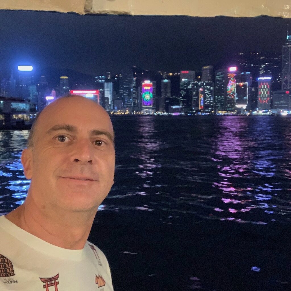 a man taking a selfie in front of a body of water with a city in the background