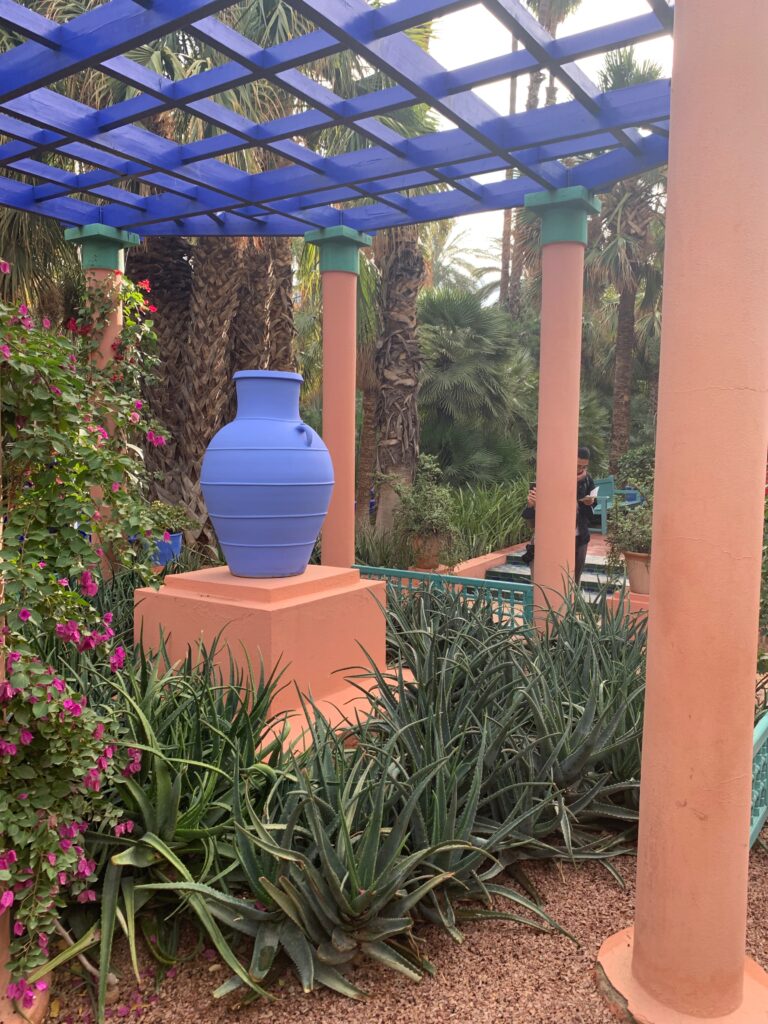 a blue vase on a pedestal surrounded by plants