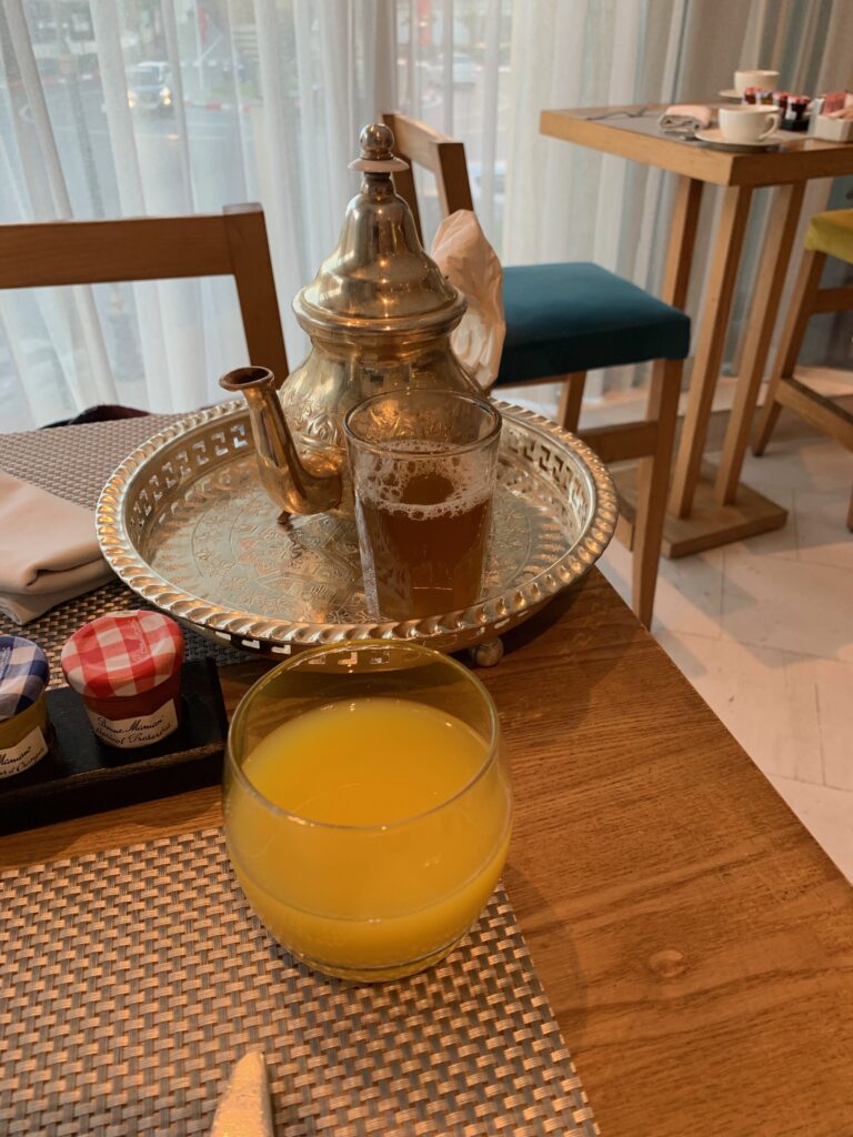 a glass of orange juice next to a metal tea kettle