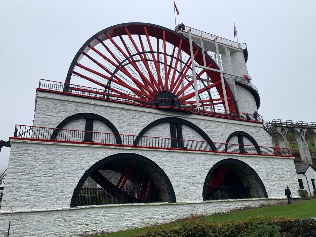 a white building with a red wheel with Arch bridge in the background