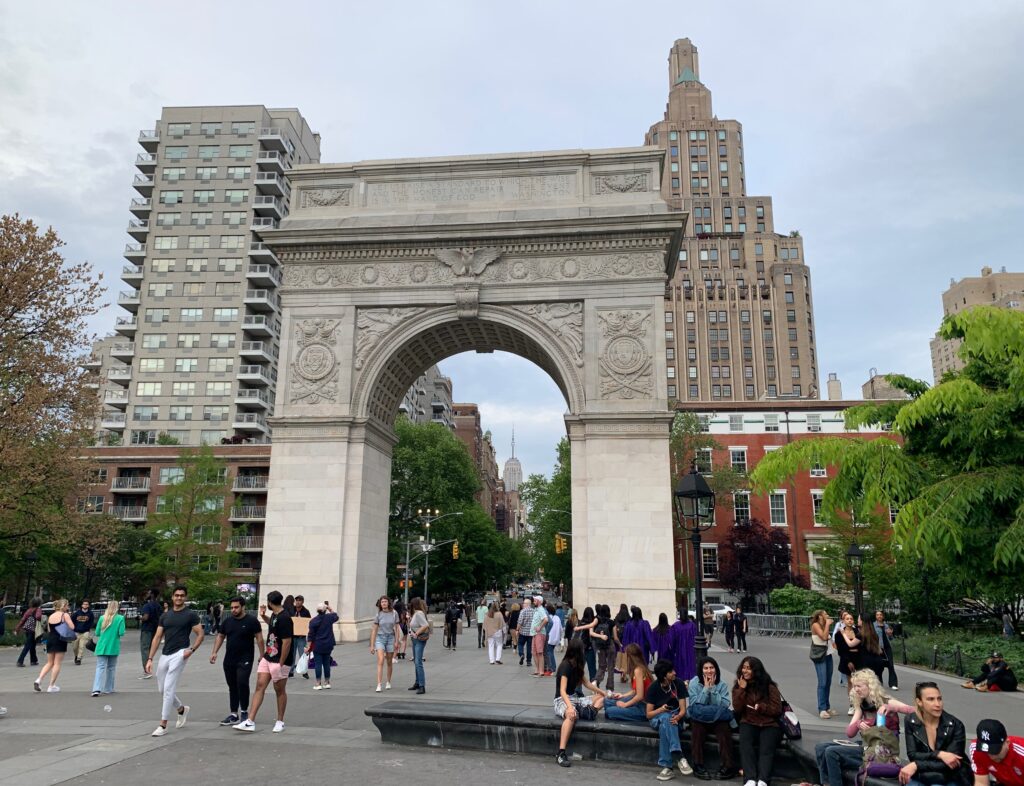 a group of people standing around a stone arch with Washington Square Park in the background