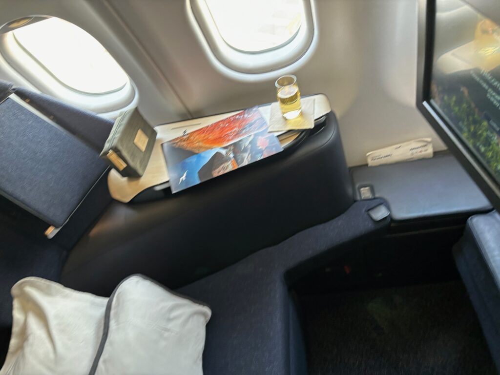 a table with a book and a drink on the side of the seat of an airplane