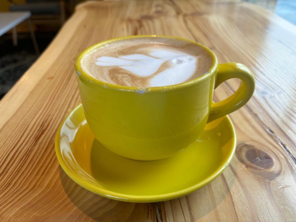 a yellow cup with a foamy drink on a saucer on a wooden table