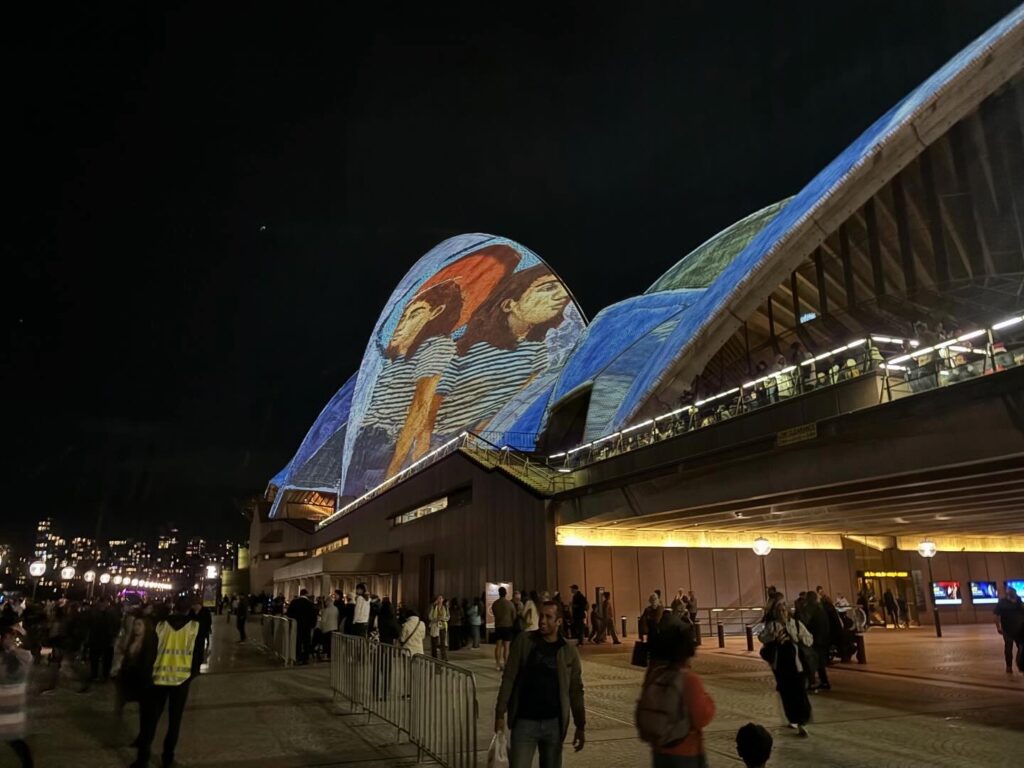 a group of people walking around a building with a large mural on the roof