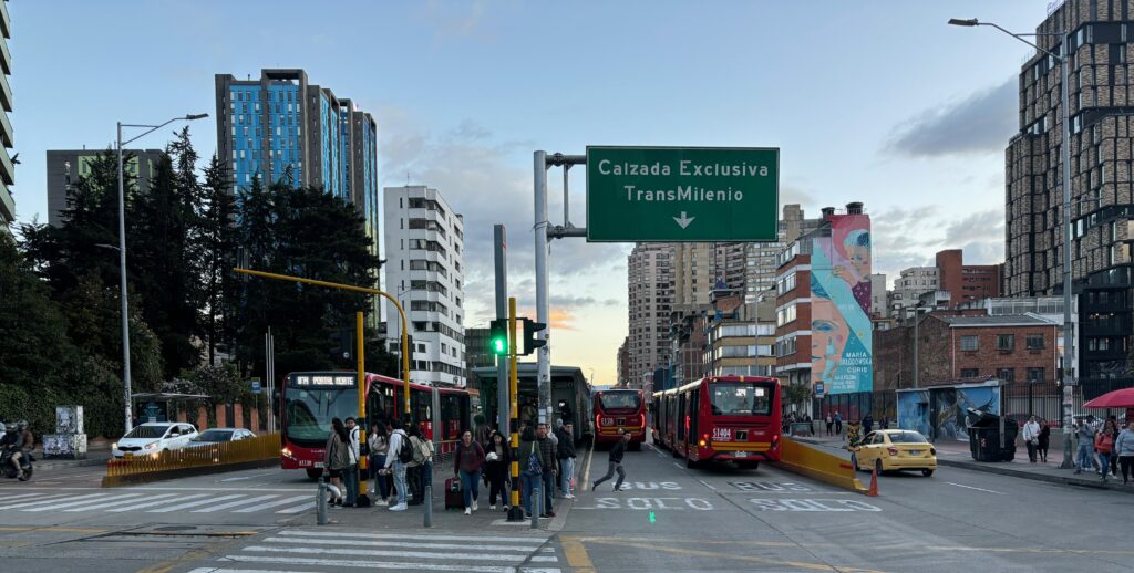 a group of people standing on a street with buses and a sign