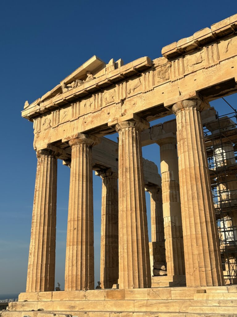 a stone structure with pillars with Parthenon in the background