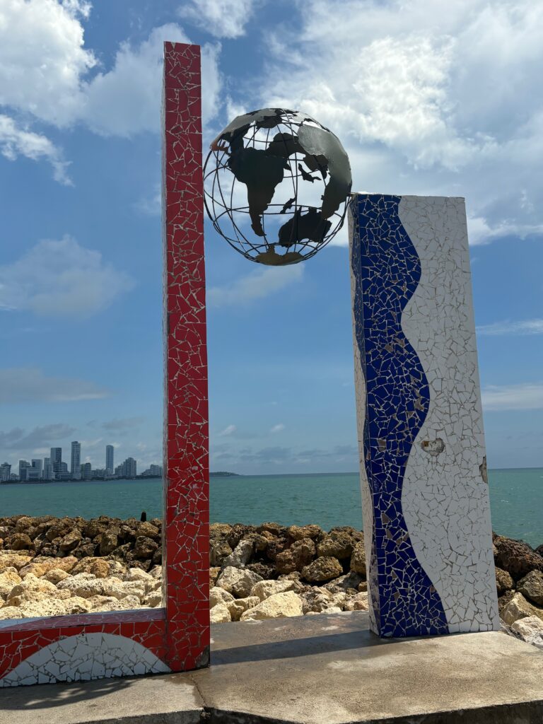 a sculpture of a globe and a red and white pole with a body of water in the background