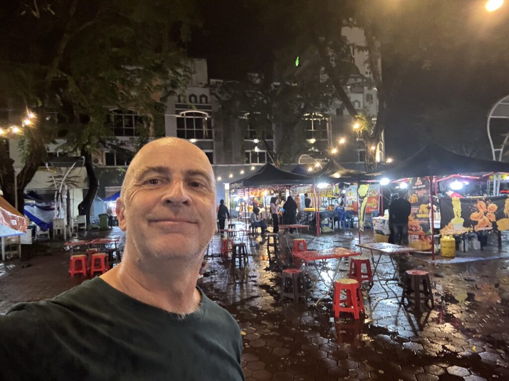 a man taking a selfie in a wet area with tables and chairs