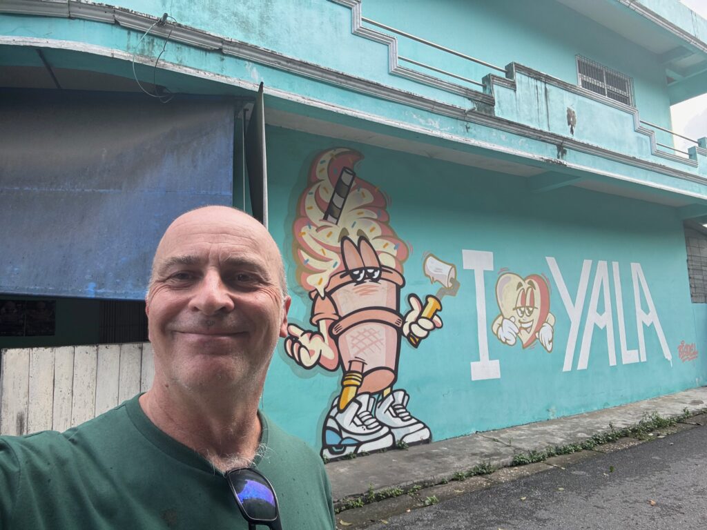 a man smiling in front of a building with graffiti