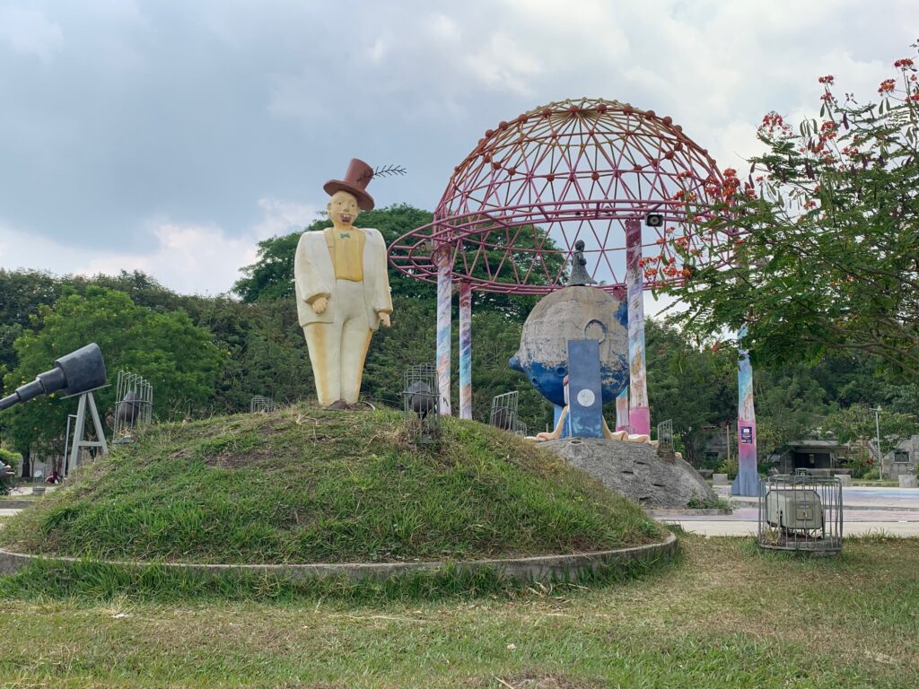 a statue of a man in a hat on a hill with a red dome and a red structure