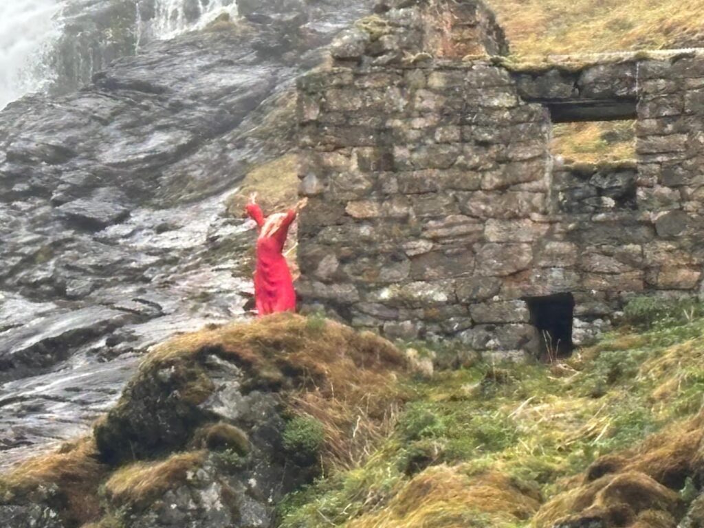 a person in a red dress standing on a rock wall