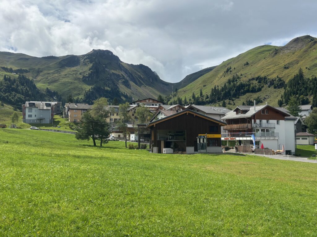 a green field with buildings and mountains in the background