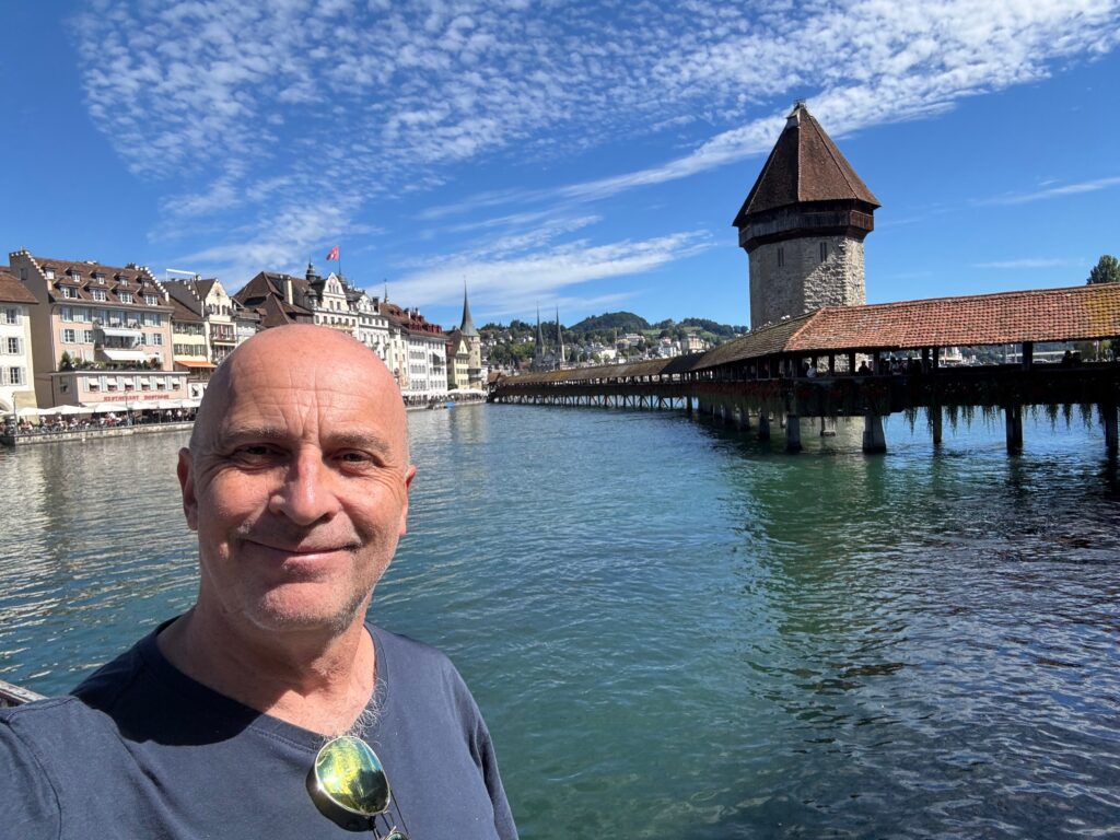 a man standing in front of water with buildings in the background with Kapellbrücke in the background