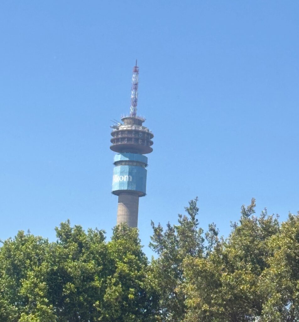 a tall tower with a blue sign and a white tower with trees in the background
