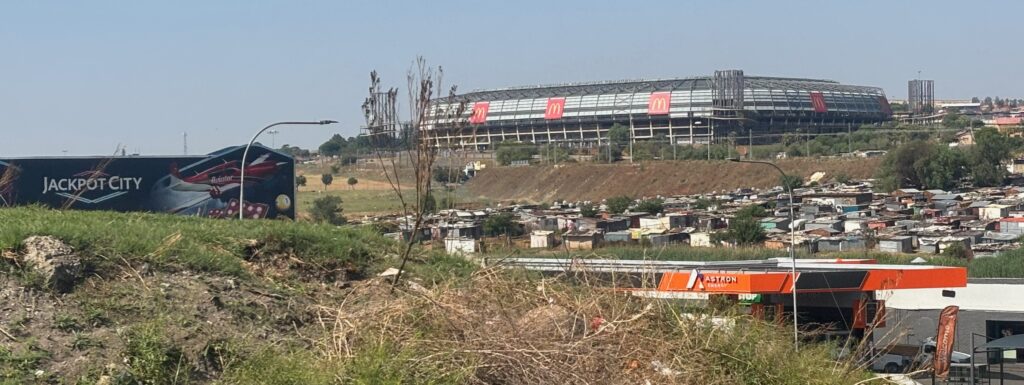 a plane flying over a field with buildings and a stadium