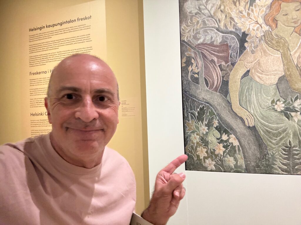 a man smiling and pointing at a painting