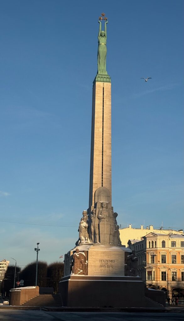 a tall tower with a bird flying in the sky with Freedom Monument in the background