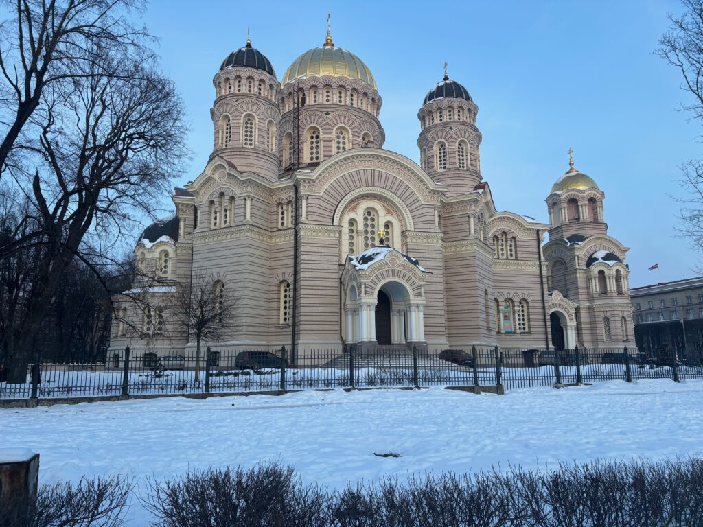 a large building with gold domes and a fence in front of it with Notre Dame d'Afrique in the background