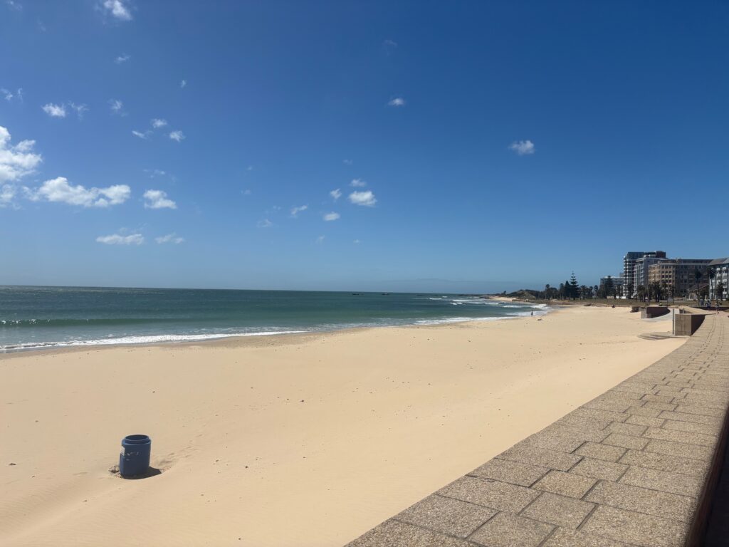 a sandy beach with blue sky and buildings