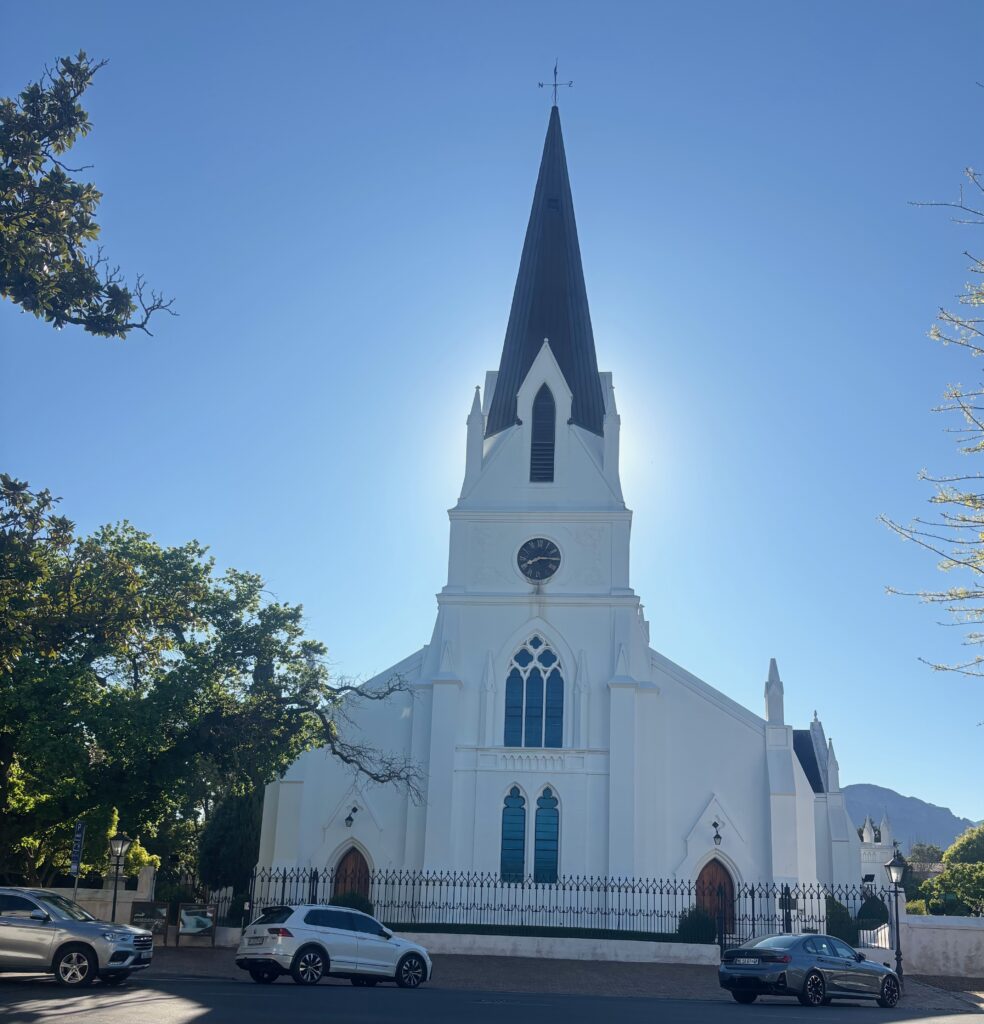 a white church with a clock tower and cars parked on the side of the road