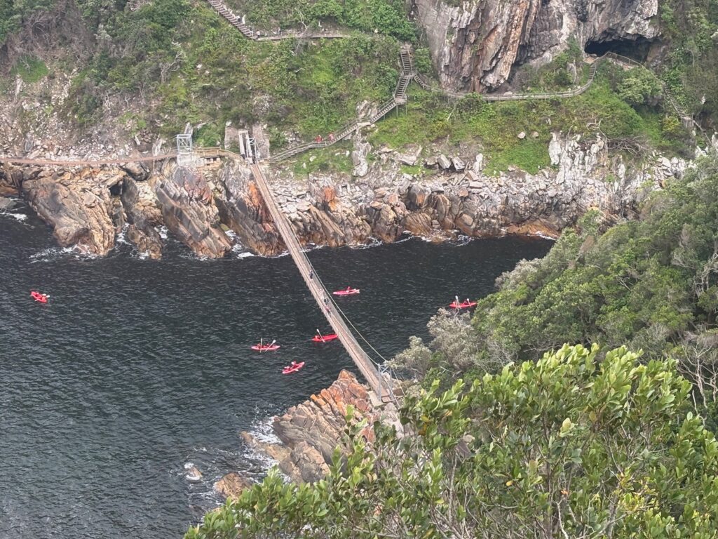 a bridge over water with kayaks and a cliff
